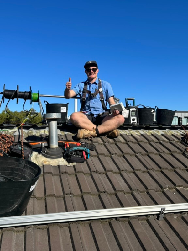 Rilan sits on a roof giving a thumbs up to contact us